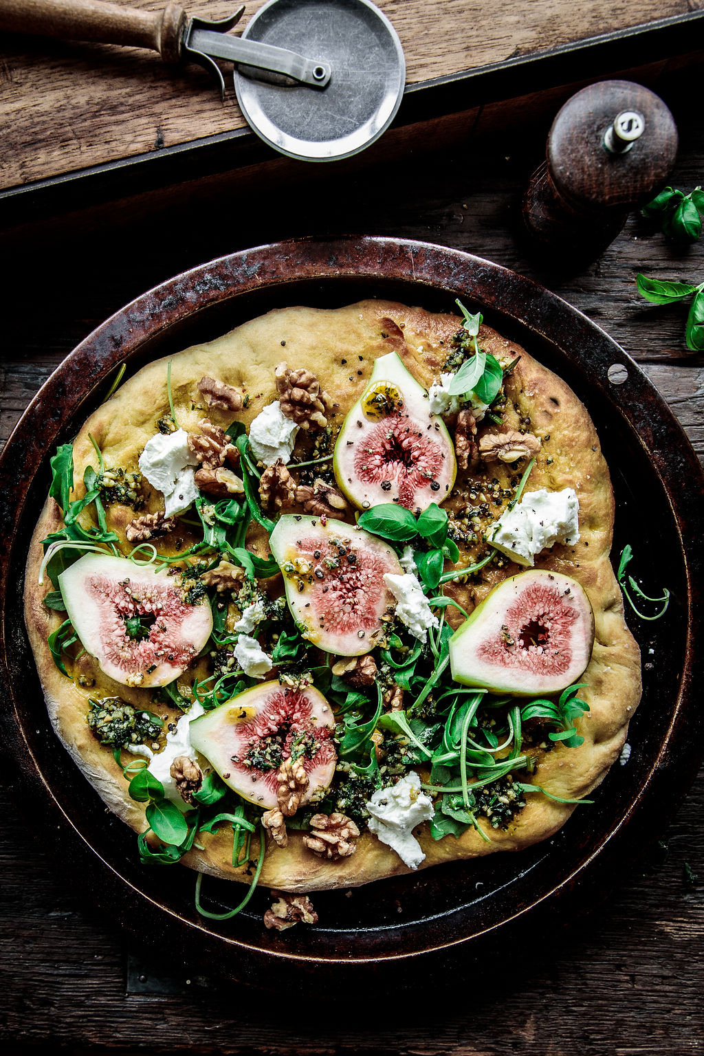 An image of a rustic home made pizza topped with walnuts, greens, and figs.